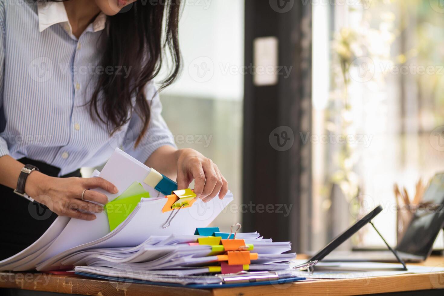 secretary is searching through pile of important documents on office table deliver them to manager for presentation in time at meeting. Concept of difficulty finding information from piles of document photo