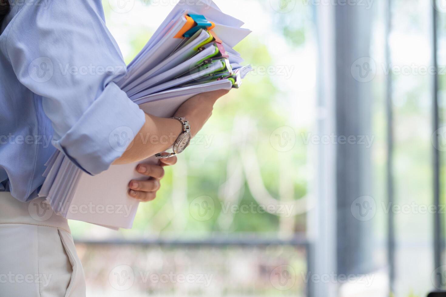 A young secretary is searching through the pile of documents on her desk to prepare for an executive meeting. The secretary looked exhausted from searching through the pile of documents on her desk. photo