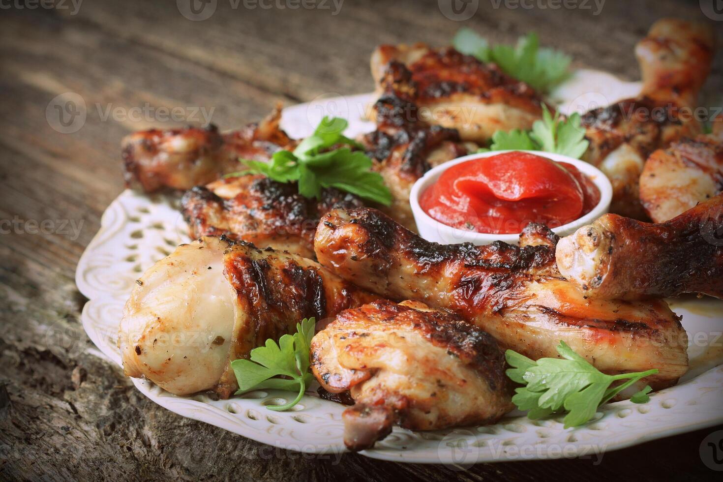 Grilled chicken legs on wooden table served on white plate with coriander photo