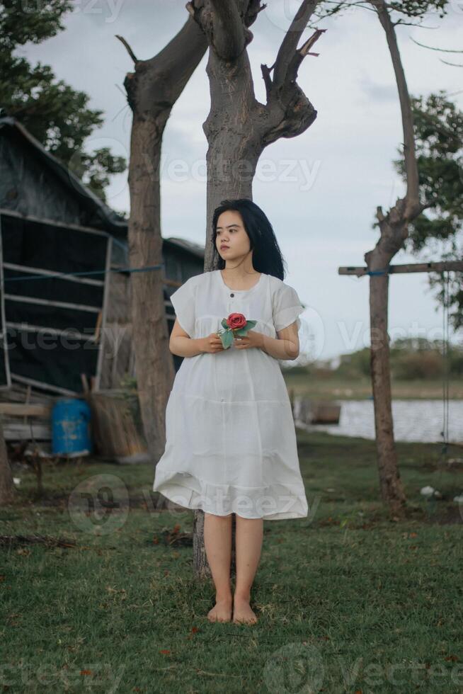 Portrait of a pretty young woman dressed in white dress holding rose flowers photo