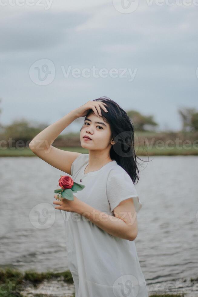 Portrait of a pretty young woman dressed in white dress holding rose flowers photo