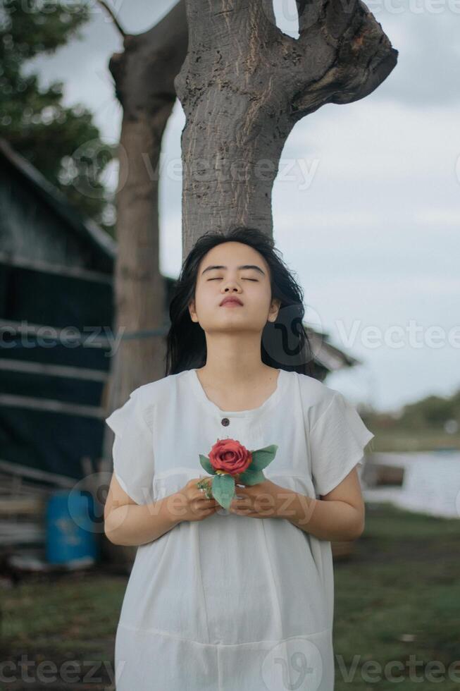 Portrait of a pretty young woman dressed in white dress holding rose flowers photo