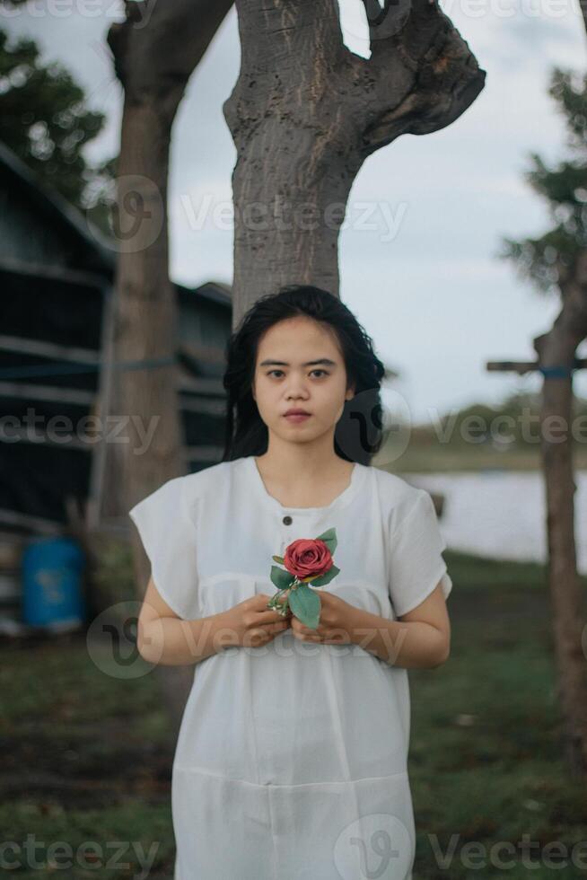 retrato de un bonito joven mujer vestido en blanco vestir participación Rosa flores foto