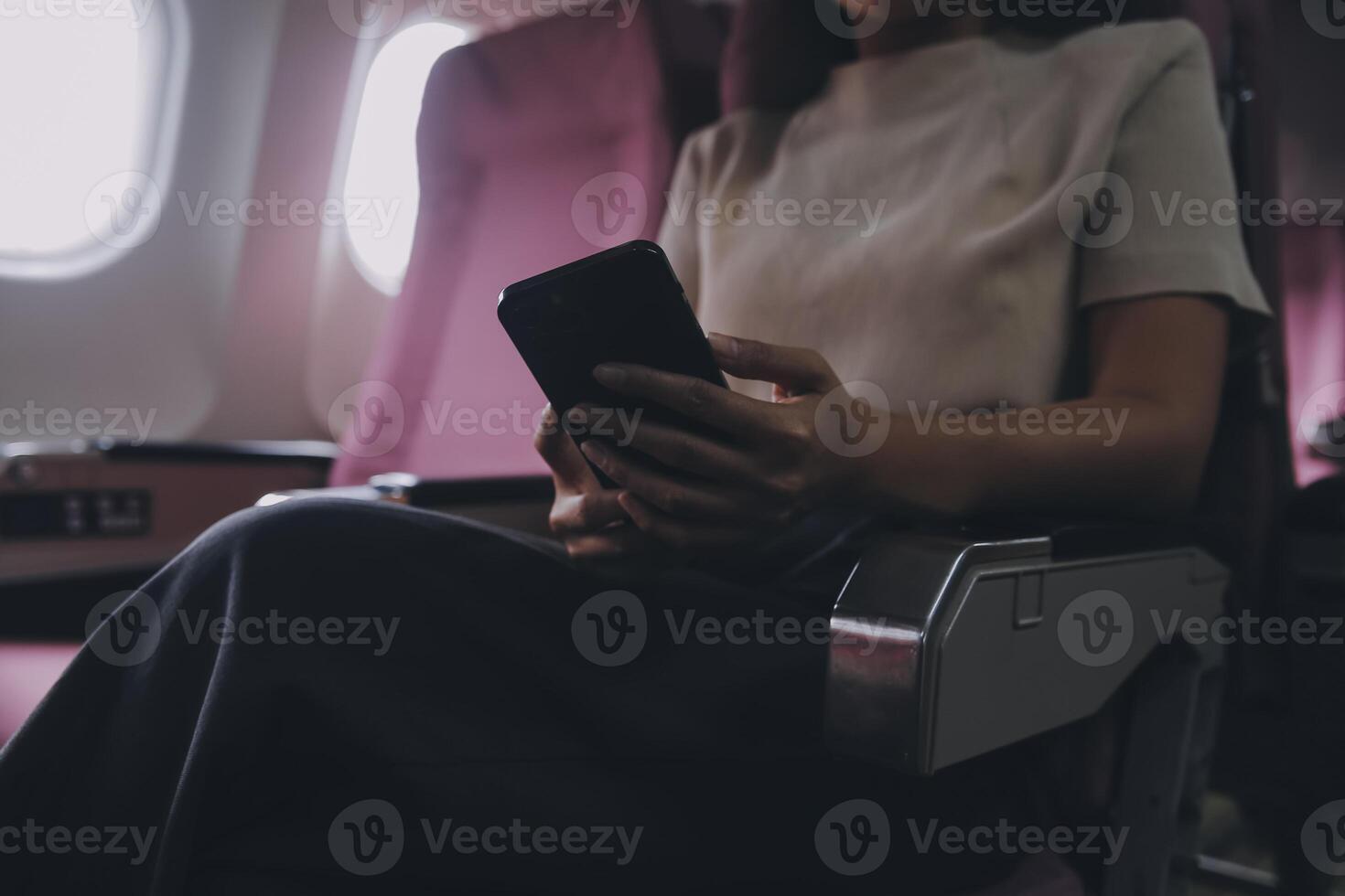 Asian woman passenger sitting in airplane near window and reading news from social networks or using travel applications in smartphone photo