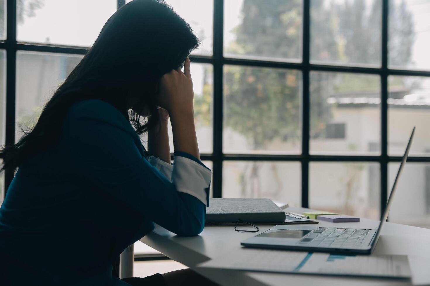 mujeres asiáticas sentadas en una oficina en casa con estrés y tensión ocular. mujer de negocios cansada sosteniendo anteojos y masajeando el puente nasal. hay tabletas, computadoras portátiles y café. foto