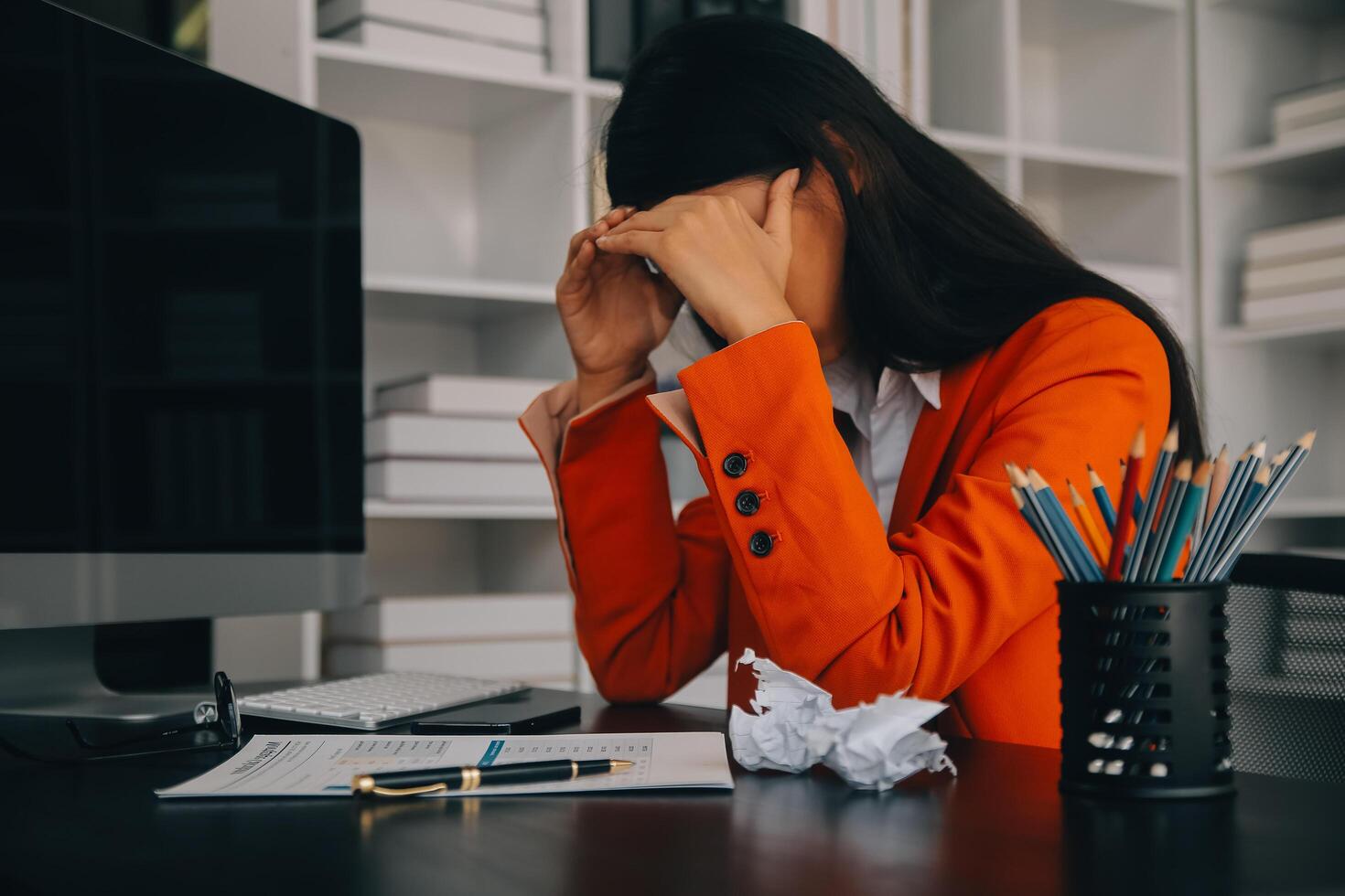 mujeres asiáticas sentadas en una oficina en casa con estrés y tensión ocular. mujer de negocios cansada sosteniendo anteojos y masajeando el puente nasal. hay tabletas, computadoras portátiles y café. foto