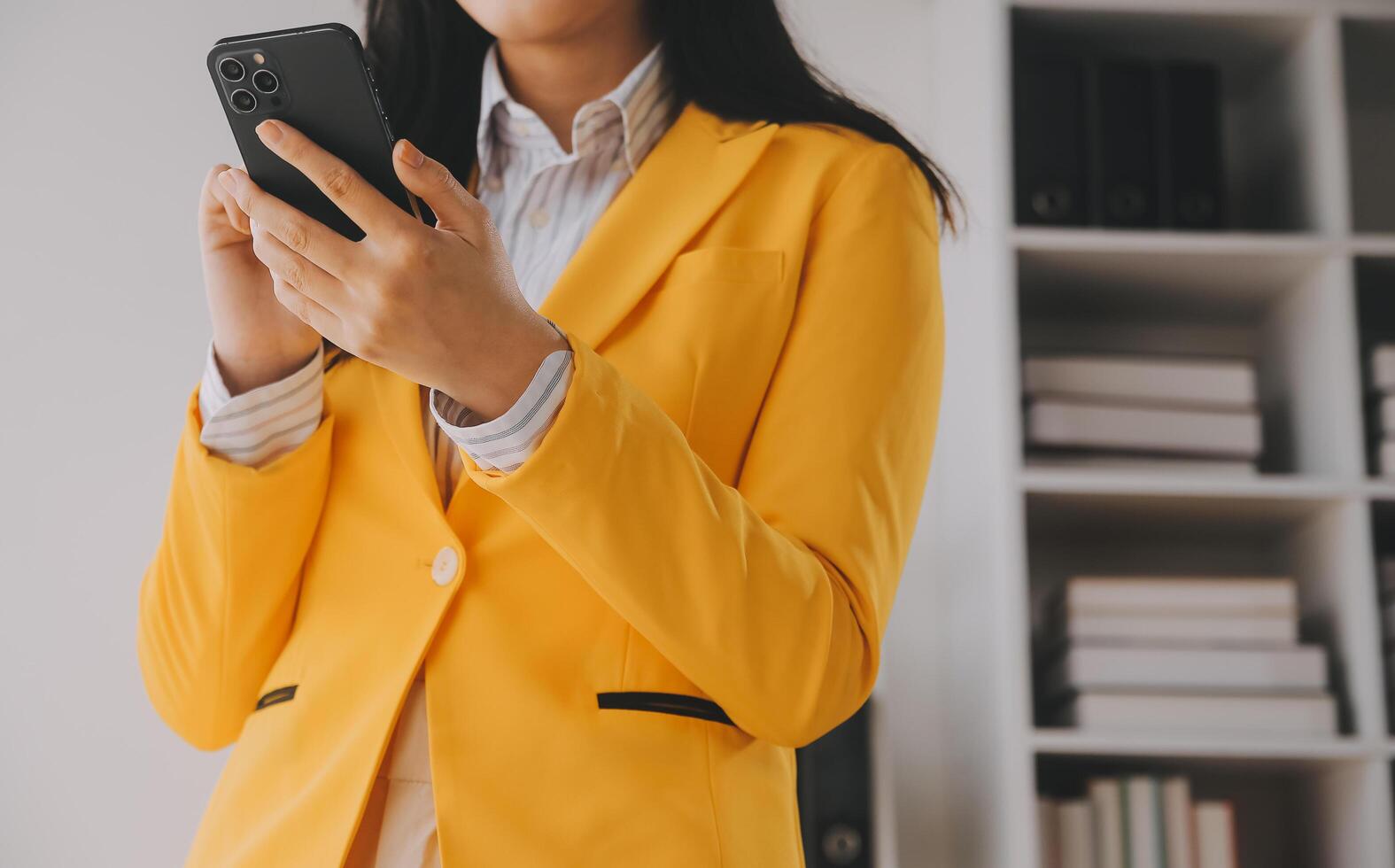 joven mujer de negocios sonriente que usa un teléfono inteligente cerca de la computadora en la oficina, copia espacio foto