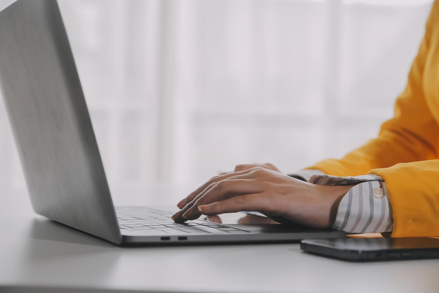 negocio mujer utilizando móvil teléfono durante trabajando en ordenador portátil computadora, surf el Internet, buscando negocio datos a moderno oficina. asiático mujer de negocios en línea trabajando en computadora a lugar de trabajo foto