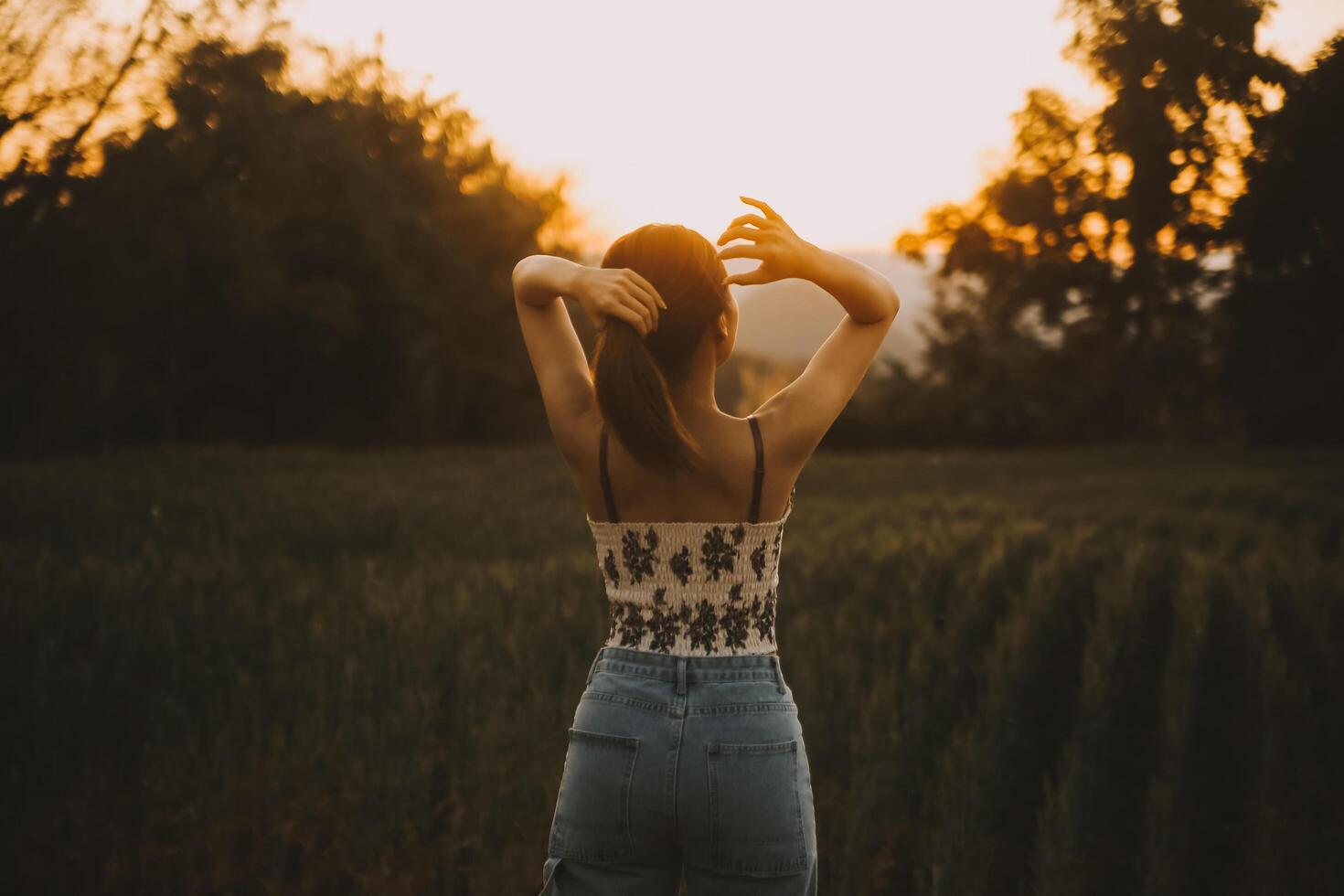 Young pretty woman in red summer dress and straw hat walking on yellow farm field with ripe golden wheat enjoying warm evening. photo