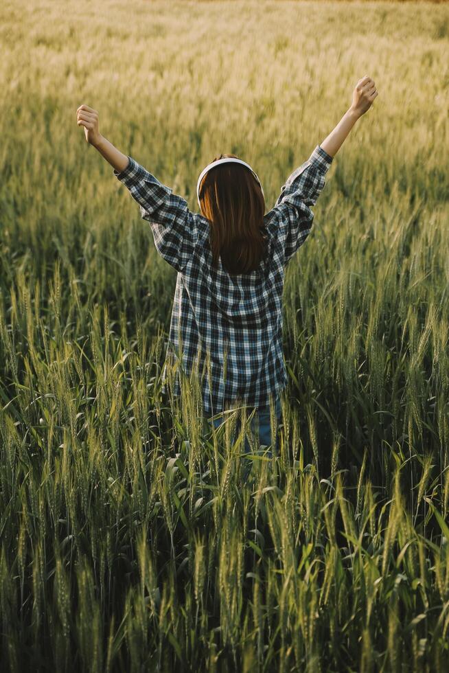 Young pretty woman in red summer dress and straw hat walking on yellow farm field with ripe golden wheat enjoying warm evening. photo