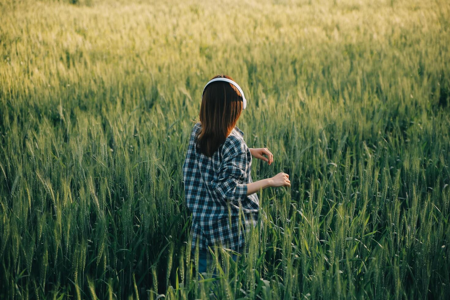 Young pretty woman in red summer dress and straw hat walking on yellow farm field with ripe golden wheat enjoying warm evening. photo