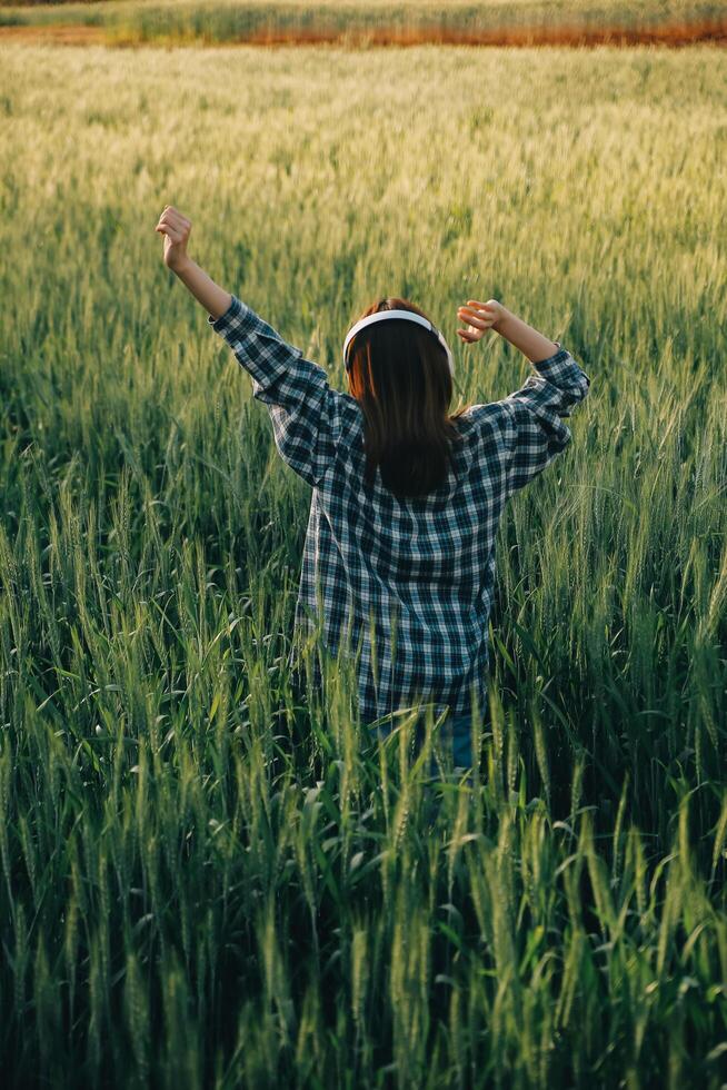 Young pretty woman in red summer dress and straw hat walking on yellow farm field with ripe golden wheat enjoying warm evening. photo