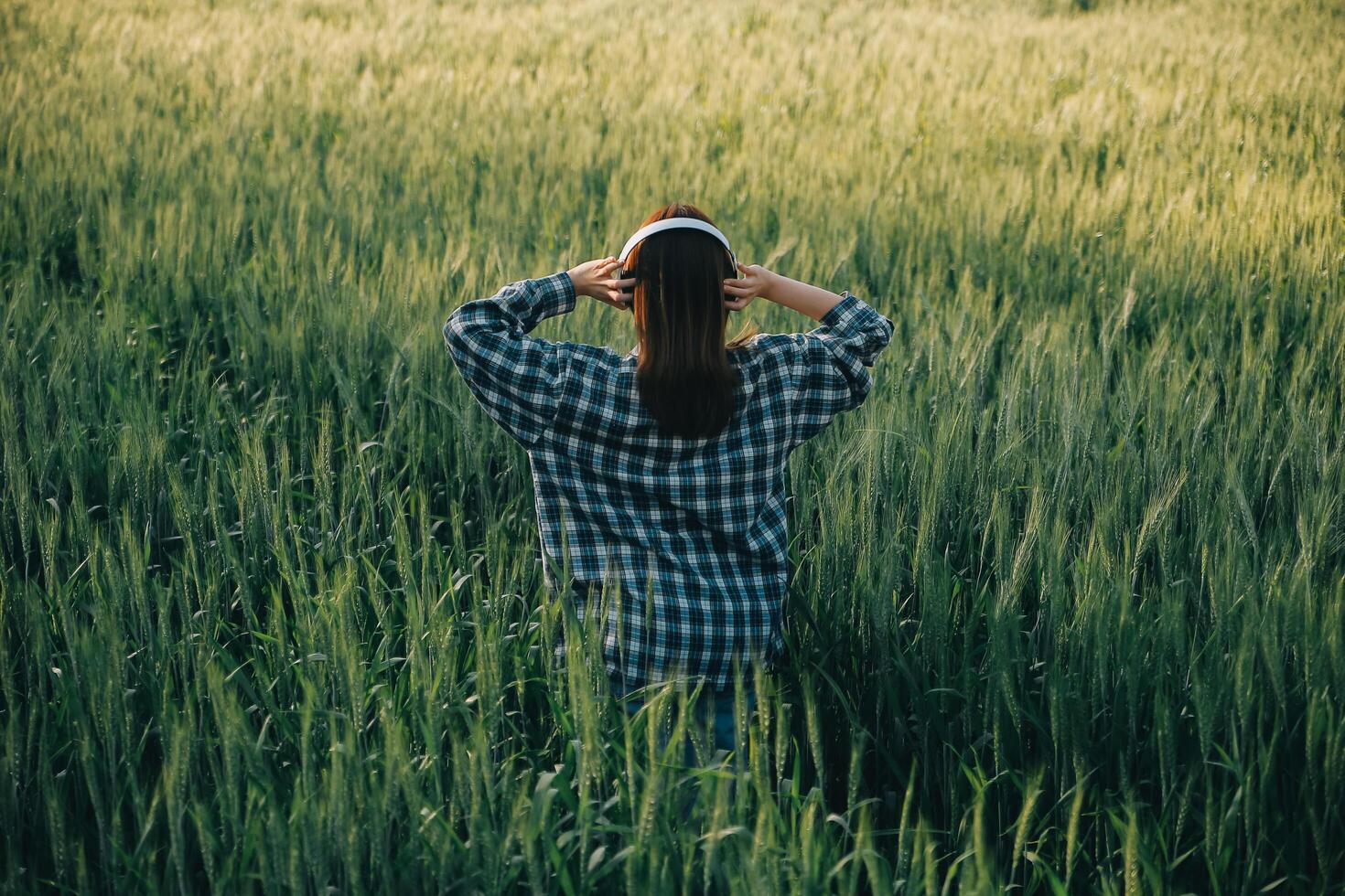 Young pretty woman in red summer dress and straw hat walking on yellow farm field with ripe golden wheat enjoying warm evening. photo