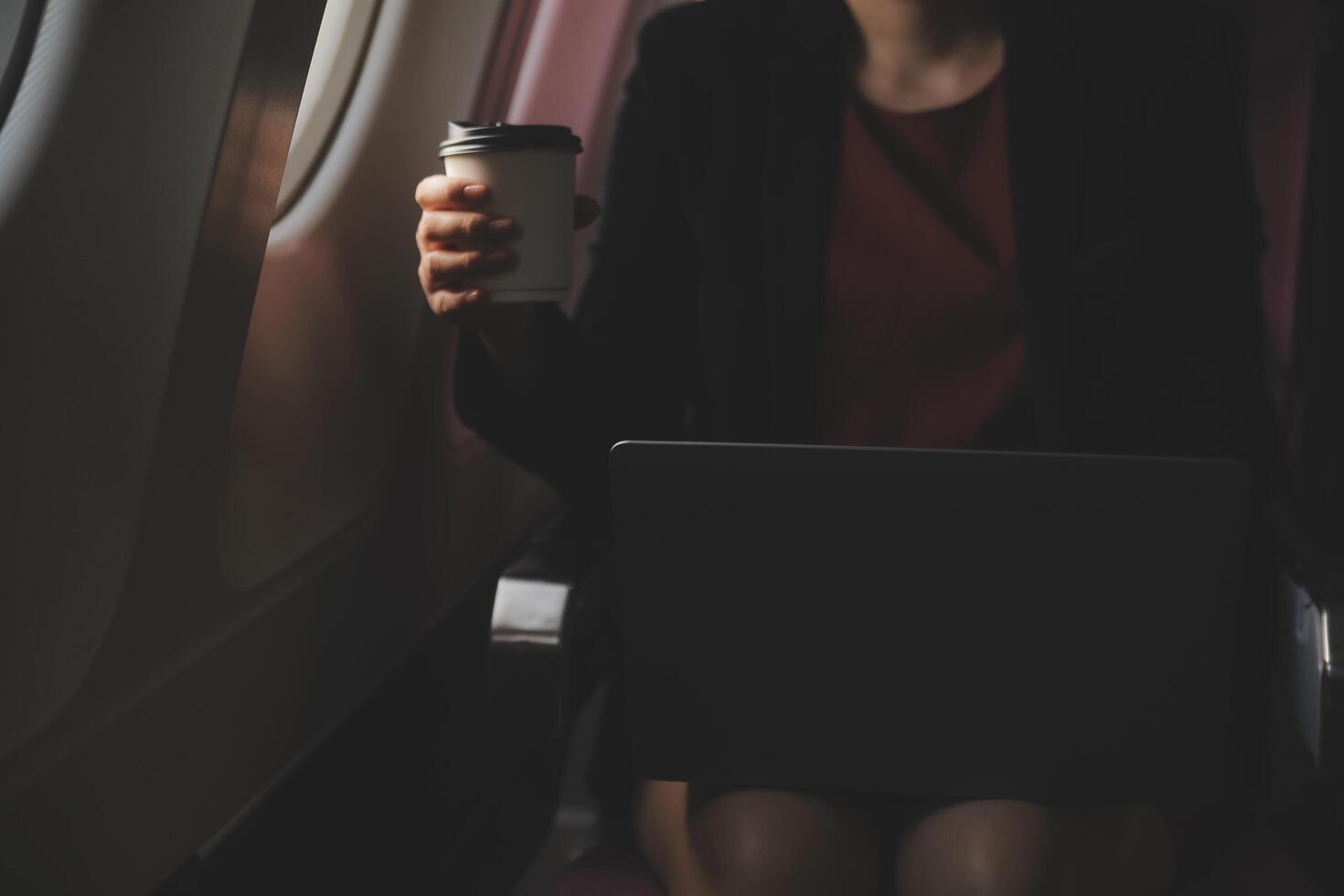 Blonde female tourist checking incoming notification on smartphone sitting on seat of airplane with netbook.Young businesswoman share media from telephone on laptop computer during plane flight photo