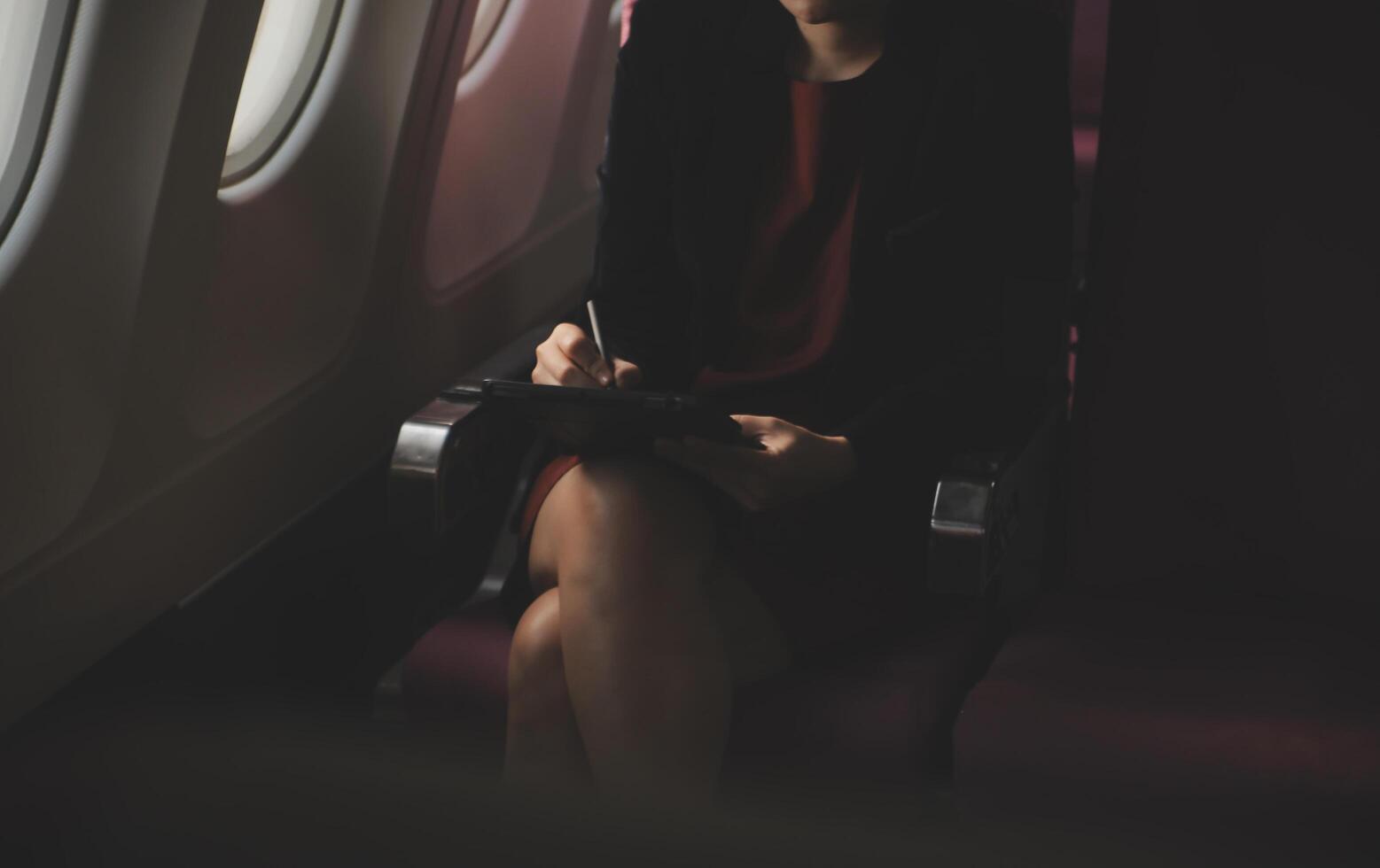 Blonde female tourist checking incoming notification on smartphone sitting on seat of airplane with netbook.Young businesswoman share media from telephone on laptop computer during plane flight photo