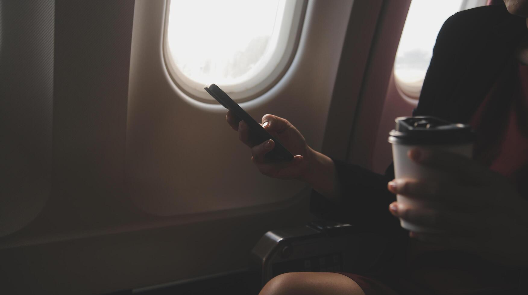 Blonde female tourist checking incoming notification on smartphone sitting on seat of airplane with netbook.Young businesswoman share media from telephone on laptop computer during plane flight photo