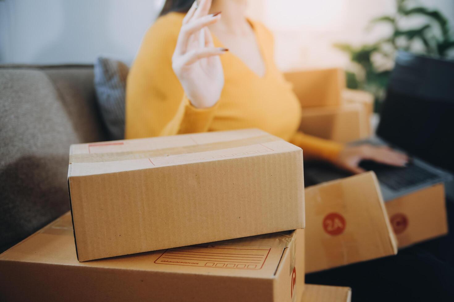 Startup small business entrepreneur or freelance Asian woman using a laptop with box, Young success Asian woman with her hand lift up, online marketing packaging box and delivery, SME concept. photo