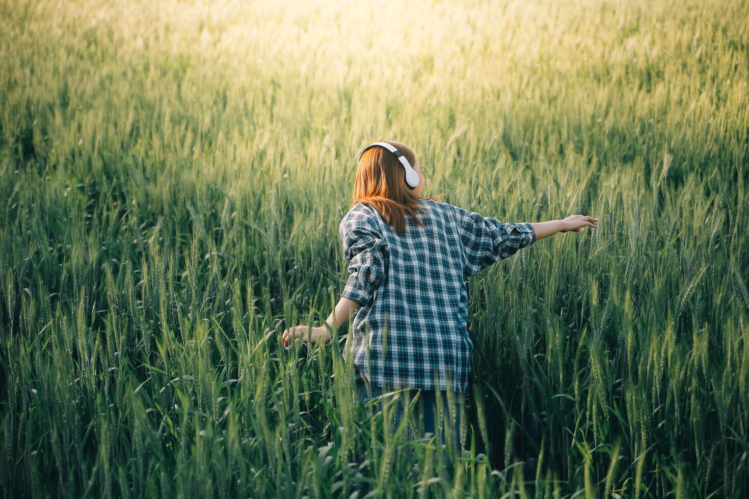 Young pretty woman in red summer dress and straw hat walking on yellow farm field with ripe golden wheat enjoying warm evening. photo