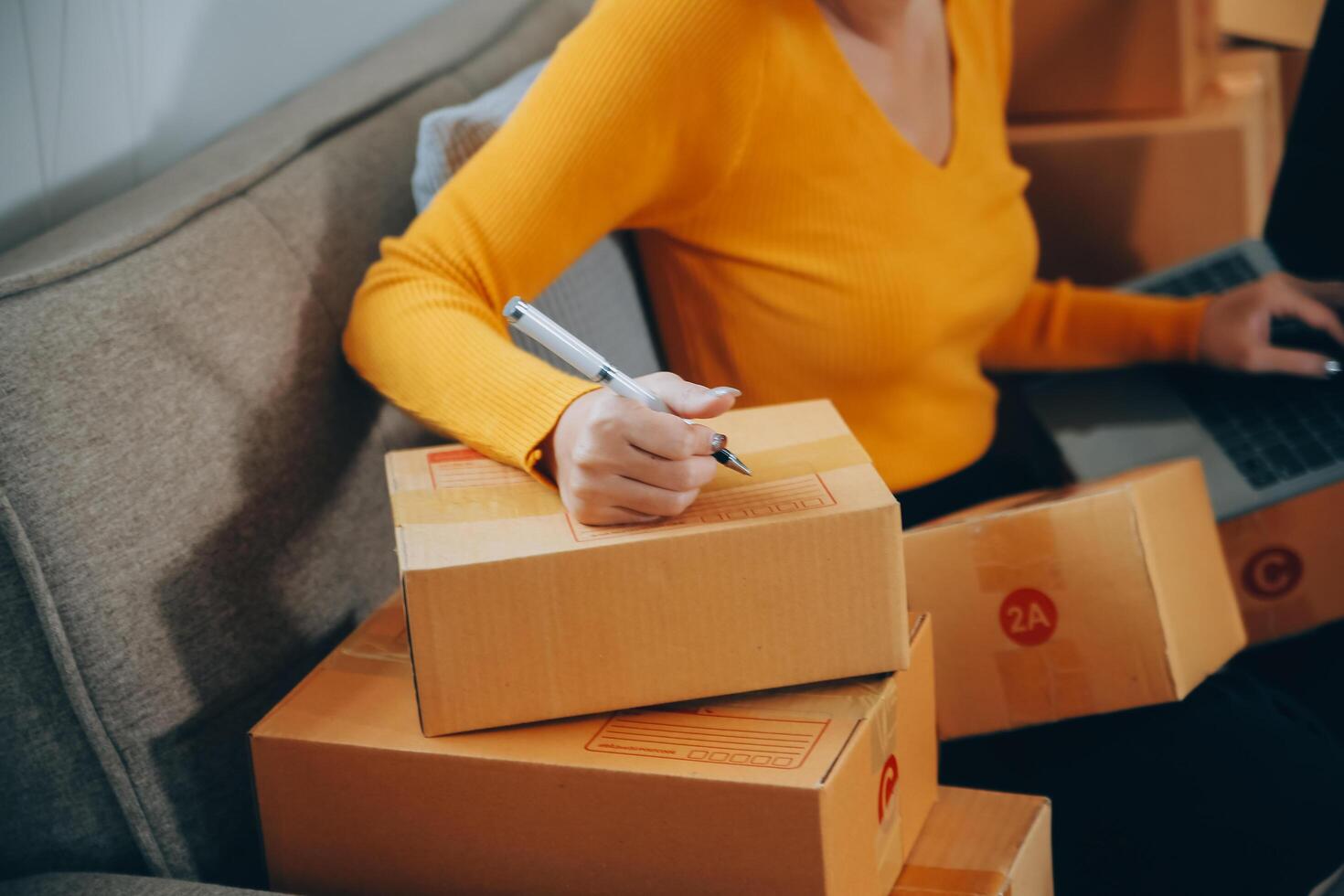 Emprendedora de pequeñas empresas o mujer asiática independiente que usa una computadora portátil con caja, joven mujer asiática de éxito con su mano levantada, caja de embalaje de marketing en línea y entrega, concepto de pyme. foto