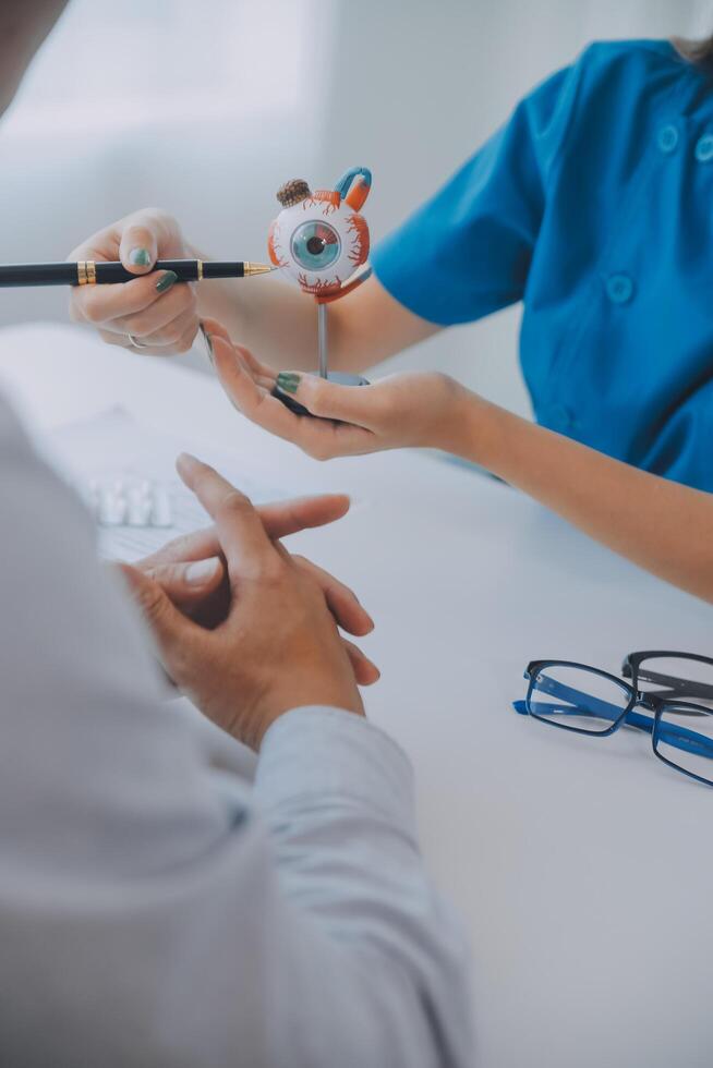 Close-up of Asian female doctor talking with elderly patient showing eyeball model and explaining eye disease in hospital photo