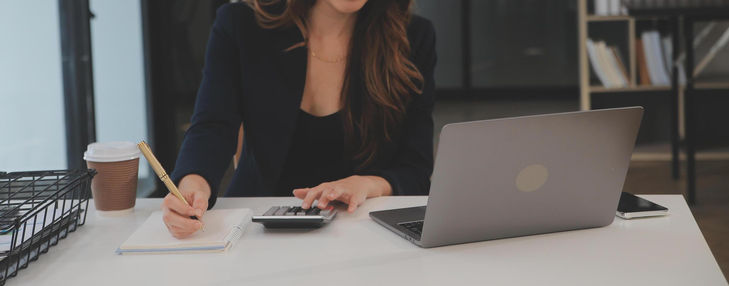 Asian Businesswoman Using laptop computer and working at office with calculator document on desk, doing planning analyzing the financial report, business plan investment, finance analysis concept. photo