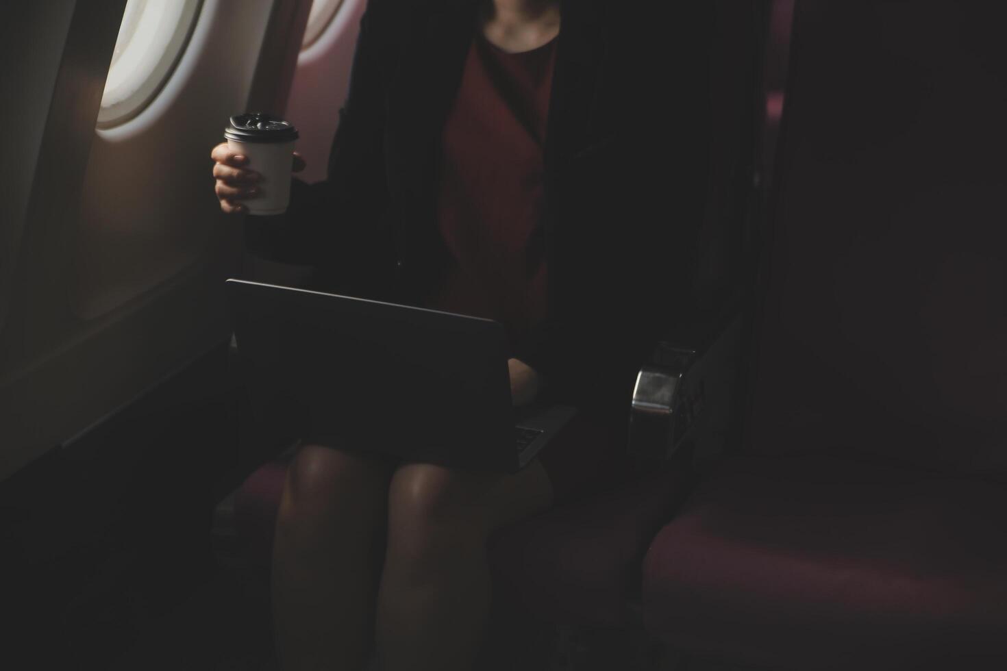 Blonde female tourist checking incoming notification on smartphone sitting on seat of airplane with netbook.Young businesswoman share media from telephone on laptop computer during plane flight photo