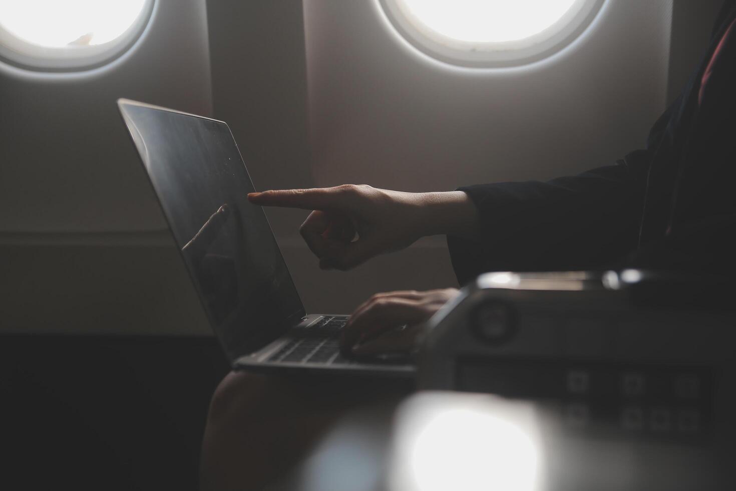 Blonde female tourist checking incoming notification on smartphone sitting on seat of airplane with netbook.Young businesswoman share media from telephone on laptop computer during plane flight photo