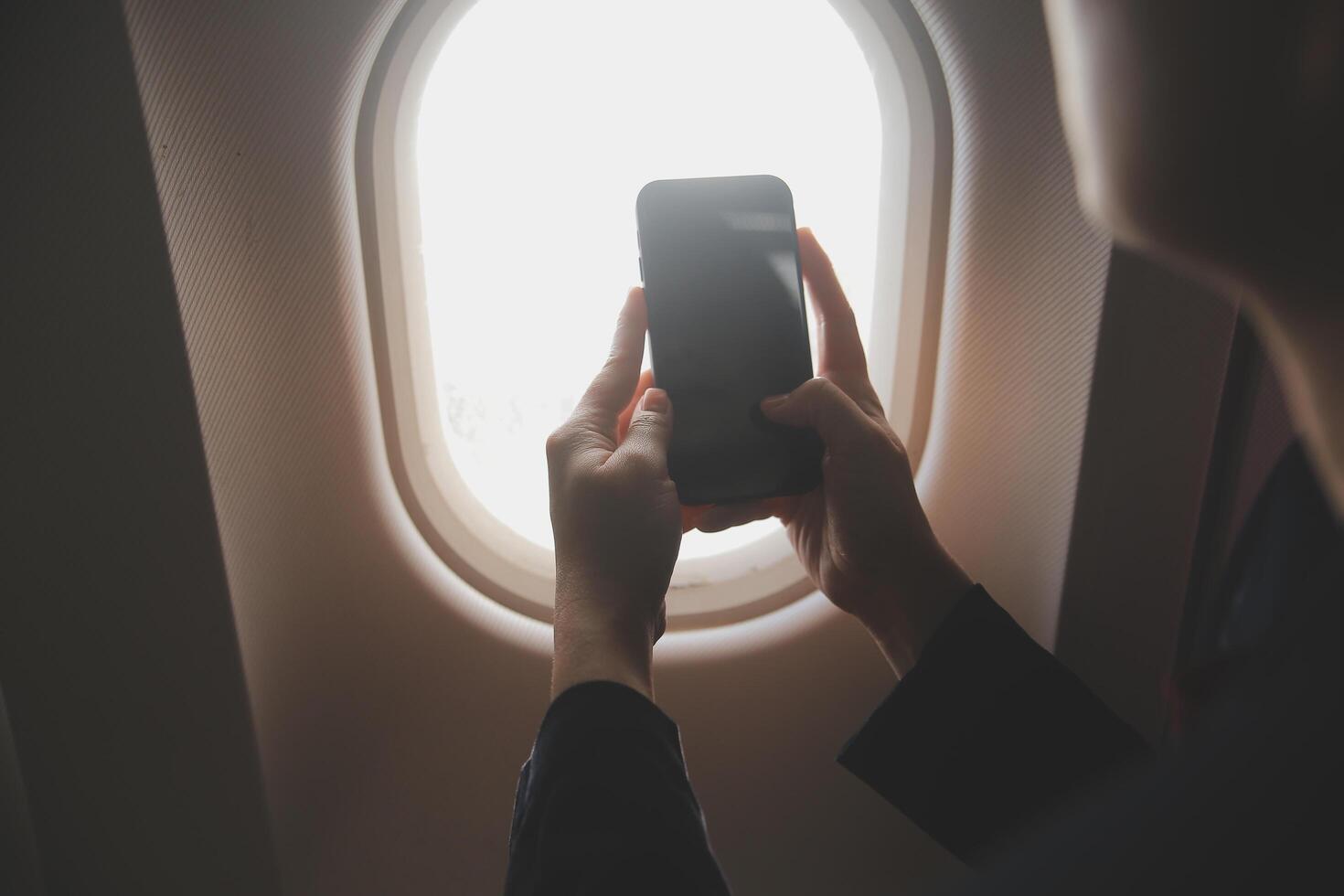 Blonde female tourist checking incoming notification on smartphone sitting on seat of airplane with netbook.Young businesswoman share media from telephone on laptop computer during plane flight photo