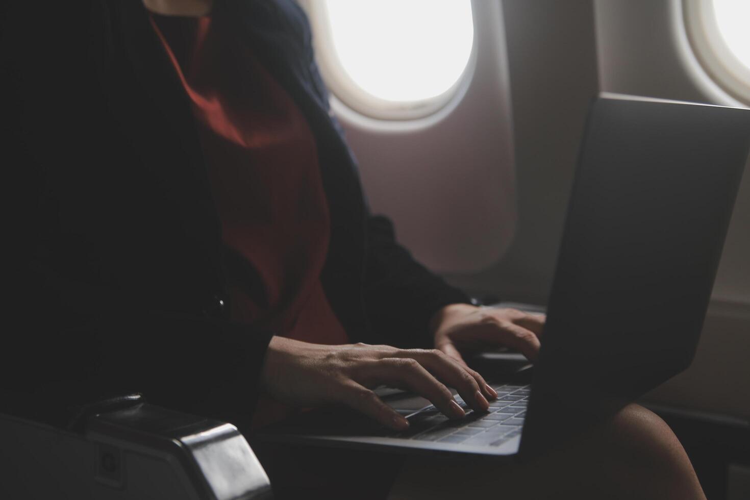 Blonde female tourist checking incoming notification on smartphone sitting on seat of airplane with netbook.Young businesswoman share media from telephone on laptop computer during plane flight photo