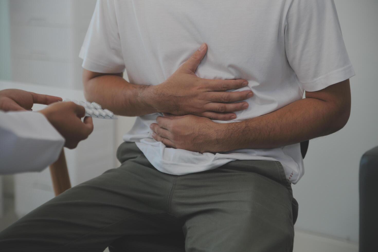 hombre sufrimiento con grave estómago dolor sentado a hogar. mano de maduro chico participación abdomen sufrimiento desde dolor, Diarrea o indigesto problema. caucásico chico prensado en barriga en doloroso sensación foto