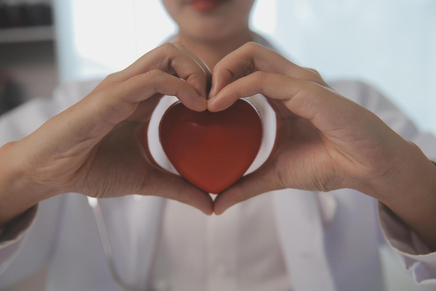 manos de médico mujer participación rojo corazón, demostración símbolo de amar, humano apoyo a paciente, promoviendo médico seguro, temprano chequeo para cuidado de la salud, cardiólogo ayuda. cerca arriba de objeto foto