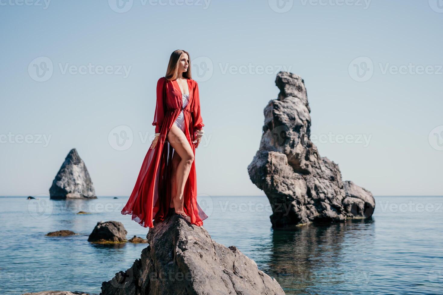 Woman travel sea. Young Happy woman in a long red dress posing on a beach near the sea on background of volcanic rocks, like in Iceland, sharing travel adventure journey photo