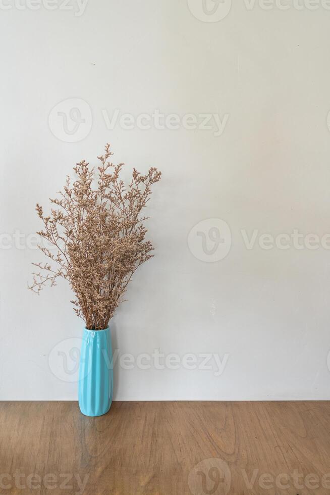 Dried flower in turquoise vase on wooden table over beige wall photo