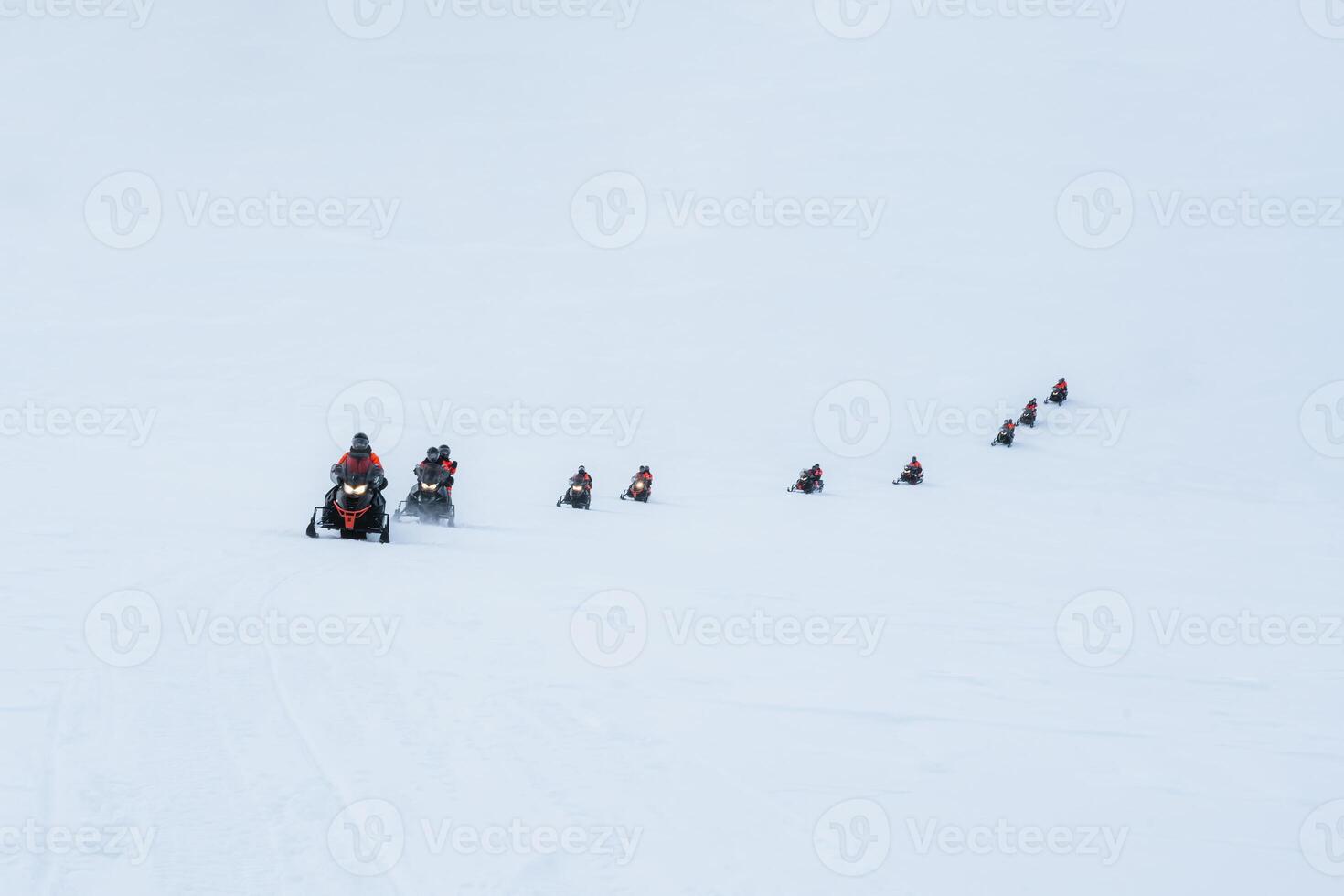 Group of tourists riding snowmobiles on snowy glacier mountain photo