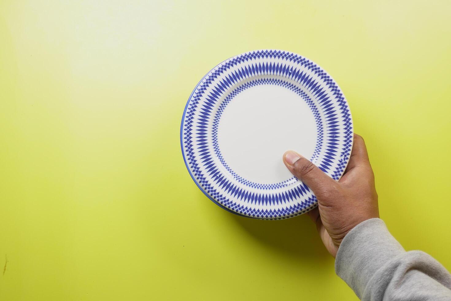 Person holds blue and white plate on yellow surface photo
