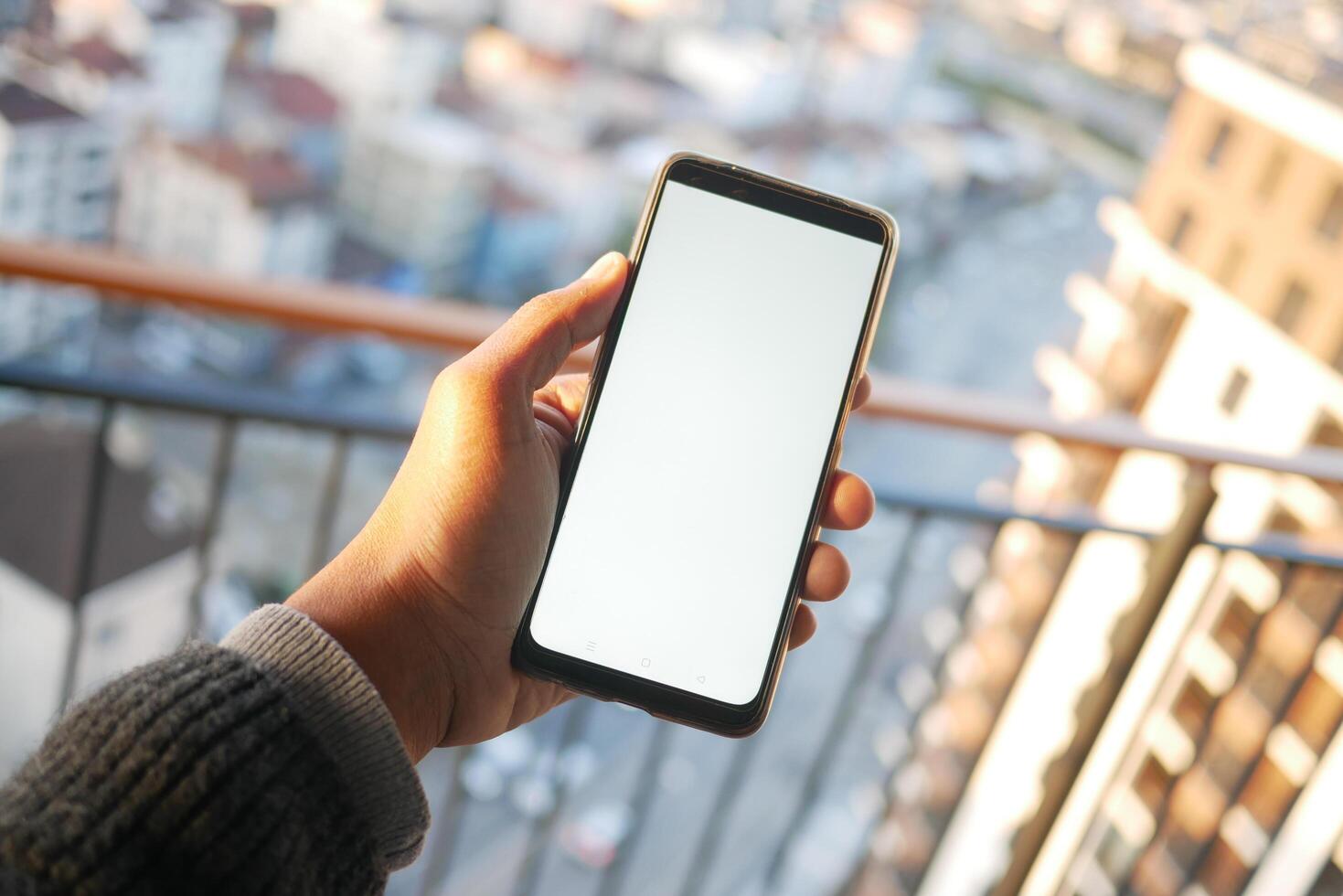 young man hand using smart phone with green screen against city buildings photo