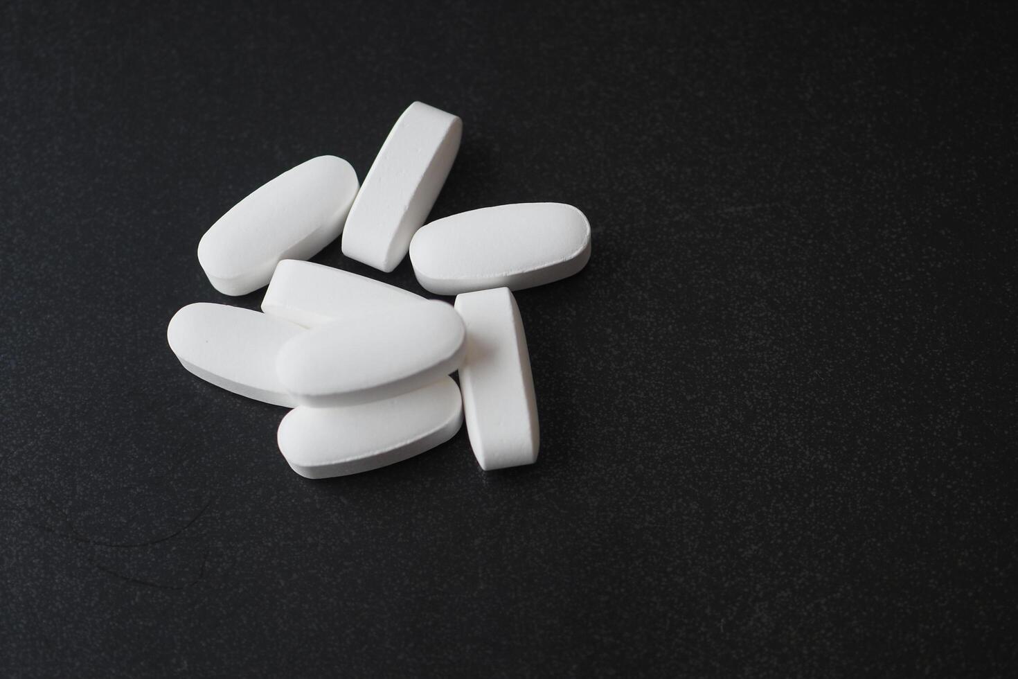 white color medical pills spilling on black background photo