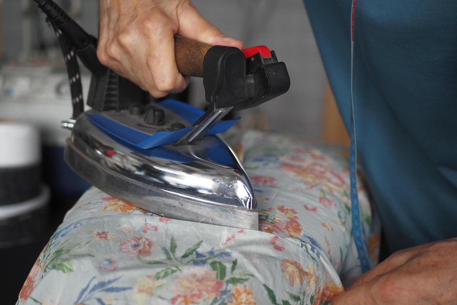 Person using electric blue iron to press floral shirt on table photo