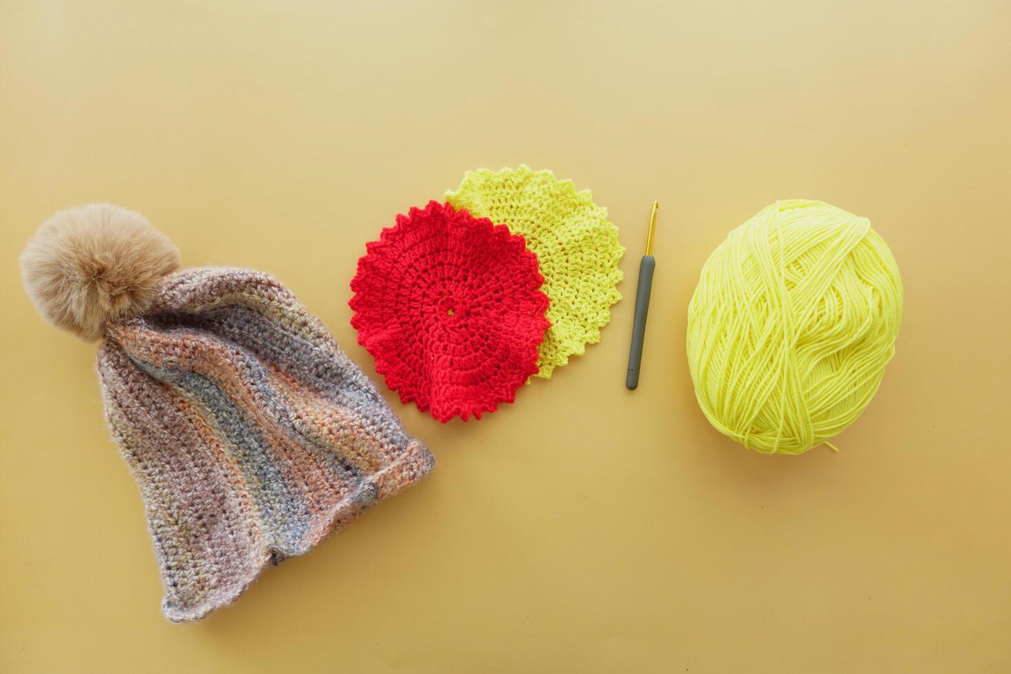 A magenta crocheted cap with woolen yarn and crochet hook displayed on table photo