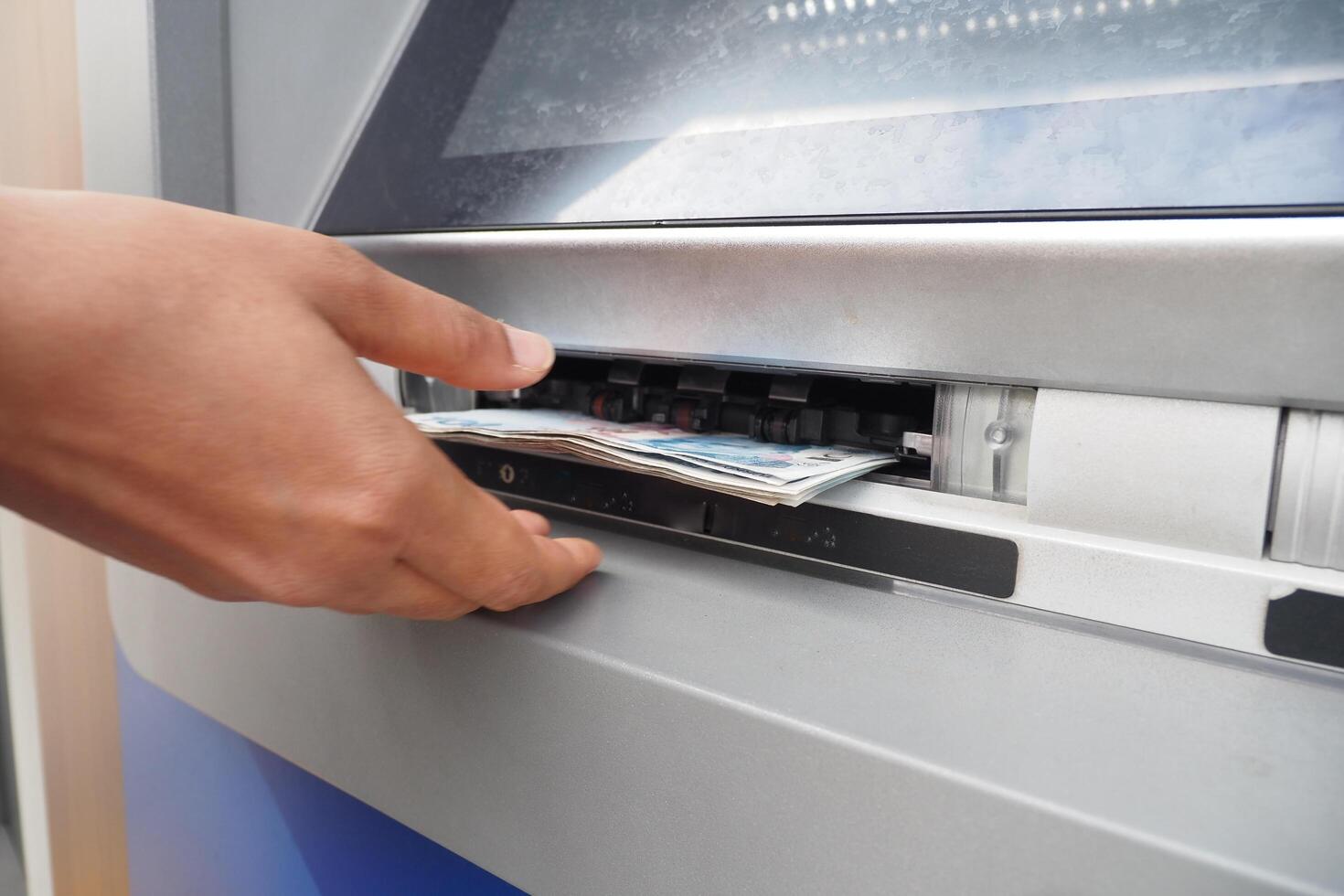 A person is withdrawing cash from an ATM machine using their thumb gesture photo