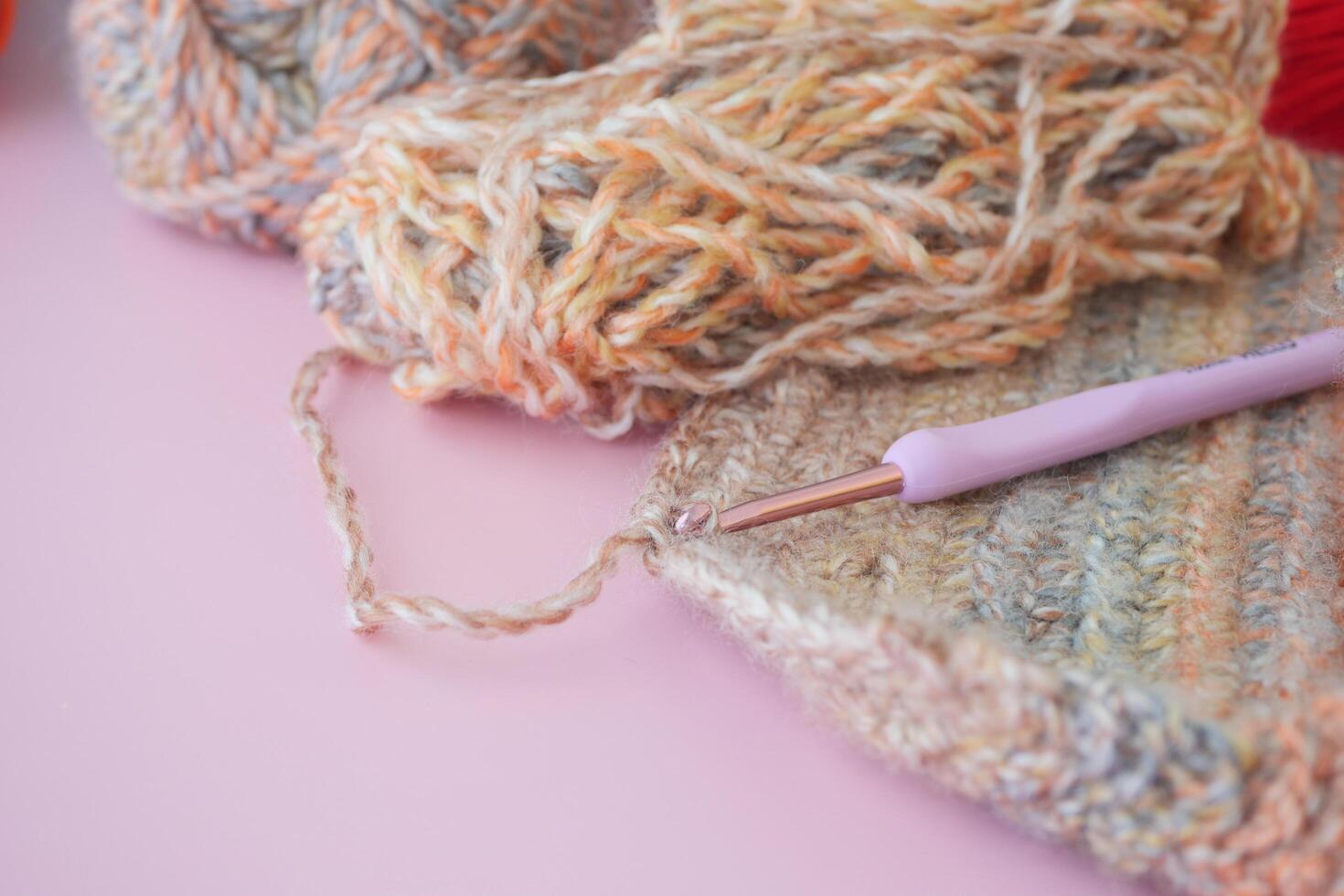a close up of a crochet hook and yarn on a pink surface photo