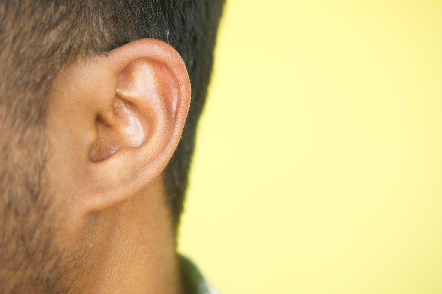 Close up of young man ear with a yellow background. photo