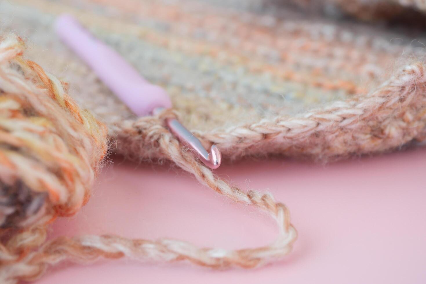 Closeup of a crochet hook and wool yarn on a magenta surface photo