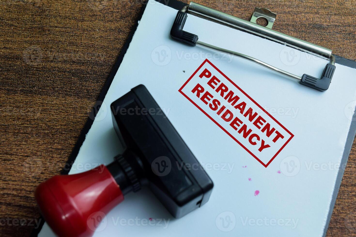 Red Handle Rubber Stamper and Permanent Residency text above book isolated on wooden background photo