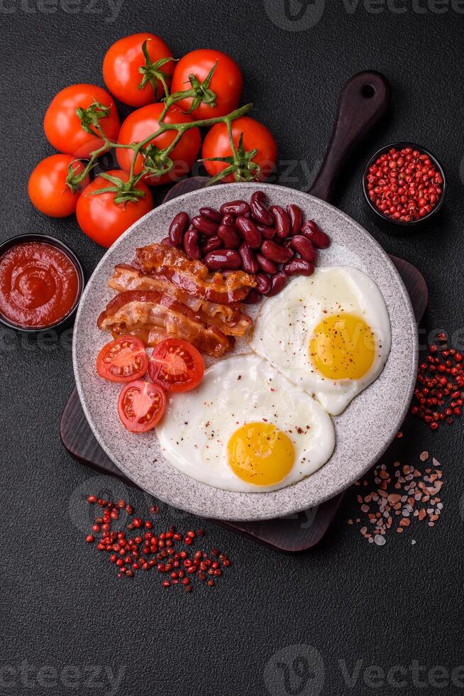 English breakfast with fried eggs, bacon, beans, tomatoes, spices and herbs photo