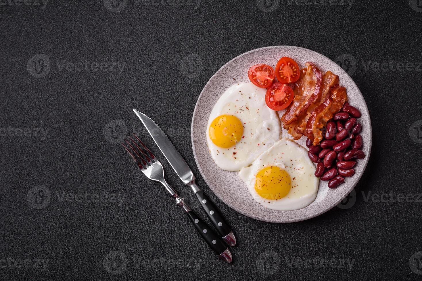 English breakfast with fried eggs, bacon, beans, tomatoes, spices and herbs photo