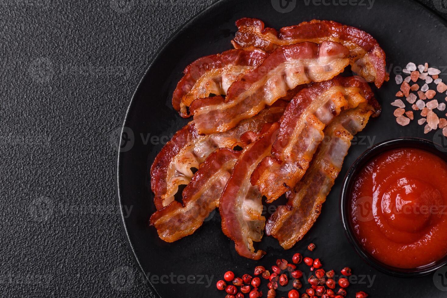 Delicious fresh fried bacon with salt and spices on a dark background photo