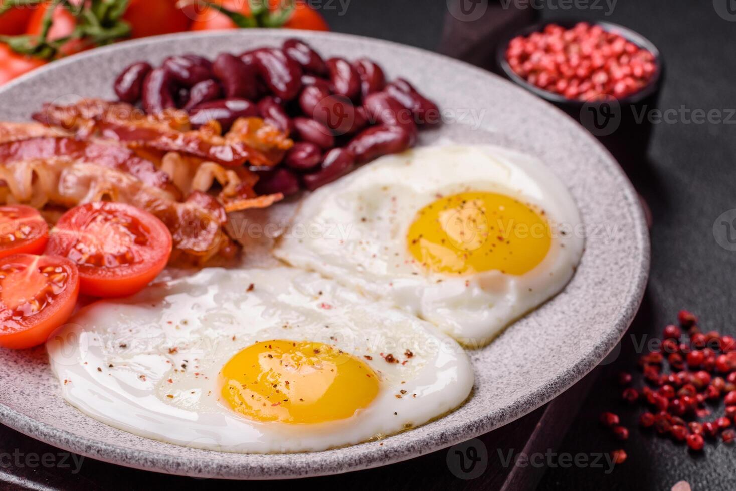 English breakfast with fried eggs, bacon, beans, tomatoes, spices and herbs photo