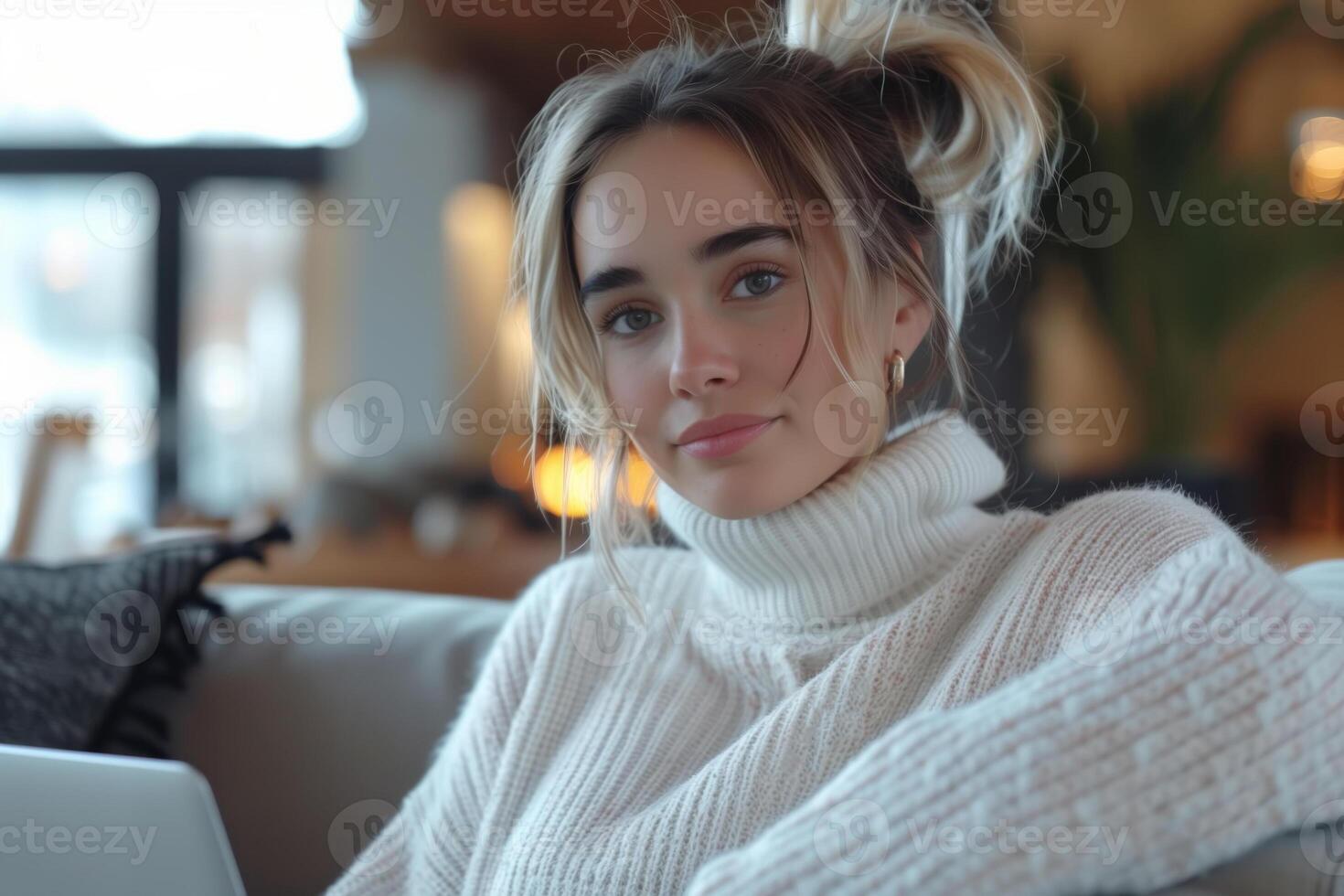 AI generated Pretty blonde woman sitting on a sofa in the living room with a laptop on her lap and looking at camera photo