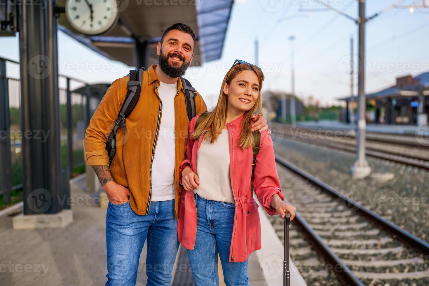 Happy couple is standing at railway station and waiting for arrival of their train. photo